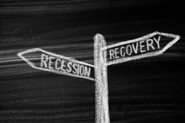 Chalk board with a sign saying recession and recovery in different directions.